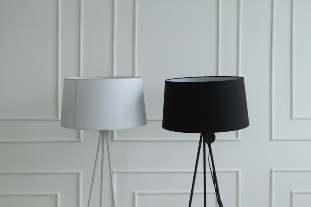 two white and black tripod lamps beside white wall