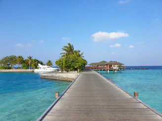 Turquoise lagoon with a wooden pier leading to a luxury villa under a clear blue sky.