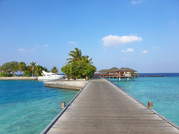 Turquoise lagoon with a wooden pier leading to a luxury villa under a clear blue sky.
