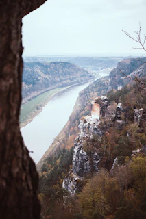 A panoramic view of a winding river cutting through a dense forest, captured from a high cliff.
