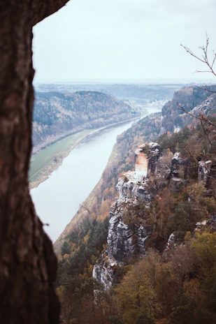 A panoramic view of a winding river cutting through a dense forest, captured from a high cliff.