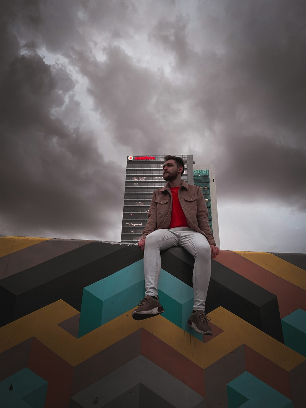 man sitting on multicolored painted wall under dark sky during daytime