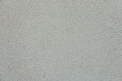 A plain, textured wall with a light, neutral tone. The surface is rough and slightly uneven, exhibiting a consistent appearance across the entire area.