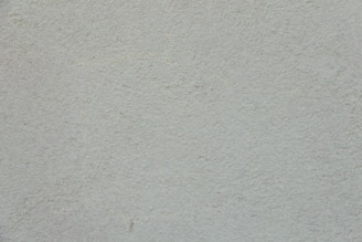 A plain, textured wall with a light, neutral tone. The surface is rough and slightly uneven, exhibiting a consistent appearance across the entire area.