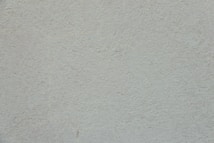 A plain, textured wall with a light, neutral tone. The surface is rough and slightly uneven, exhibiting a consistent appearance across the entire area.