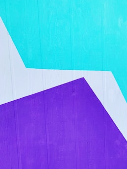 A wall painted with geometric shapes in bright turquoise, purple, and white colors. The texture of the wood is visible underneath the paint.