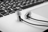 Close-up of headphones resting on a keyboard with a glowing playlist on a laptop screen.