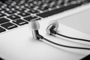 Close-up of headphones resting on a keyboard with a glowing playlist on a laptop screen.