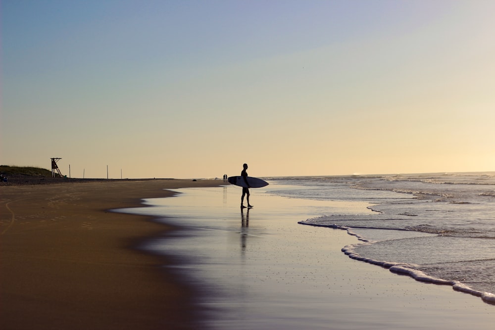 personas que sostienen una tabla de surf de pie en la orilla del mar durante el día