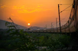 Vintage steam locomotive chugging through a rugged western landscape at sunset.