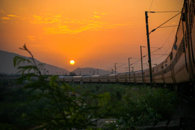 A vibrant sunset over a vintage train winding through lush green hills.