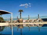 A serene hotel pool area with loungers and palm trees under a bright blue sky.
