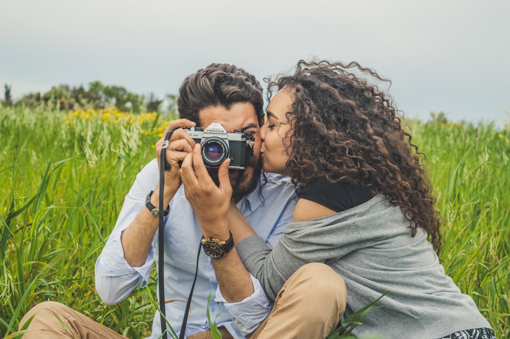 man and woman sitting on grass field holding camera