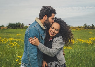 man kissing on woman's head on the green grassy field