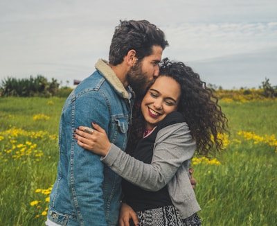 man kissing on woman's head on the green grassy field