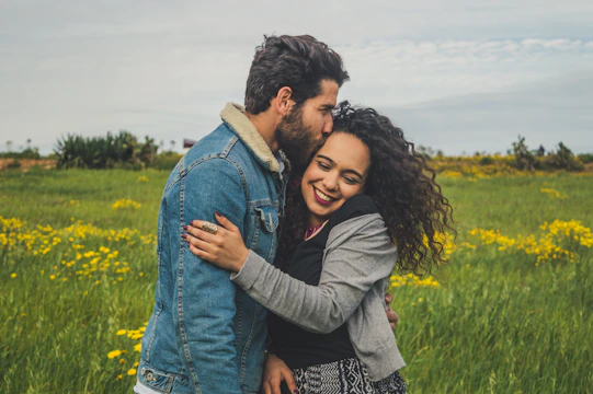 man kissing on woman's head on the green grassy field
