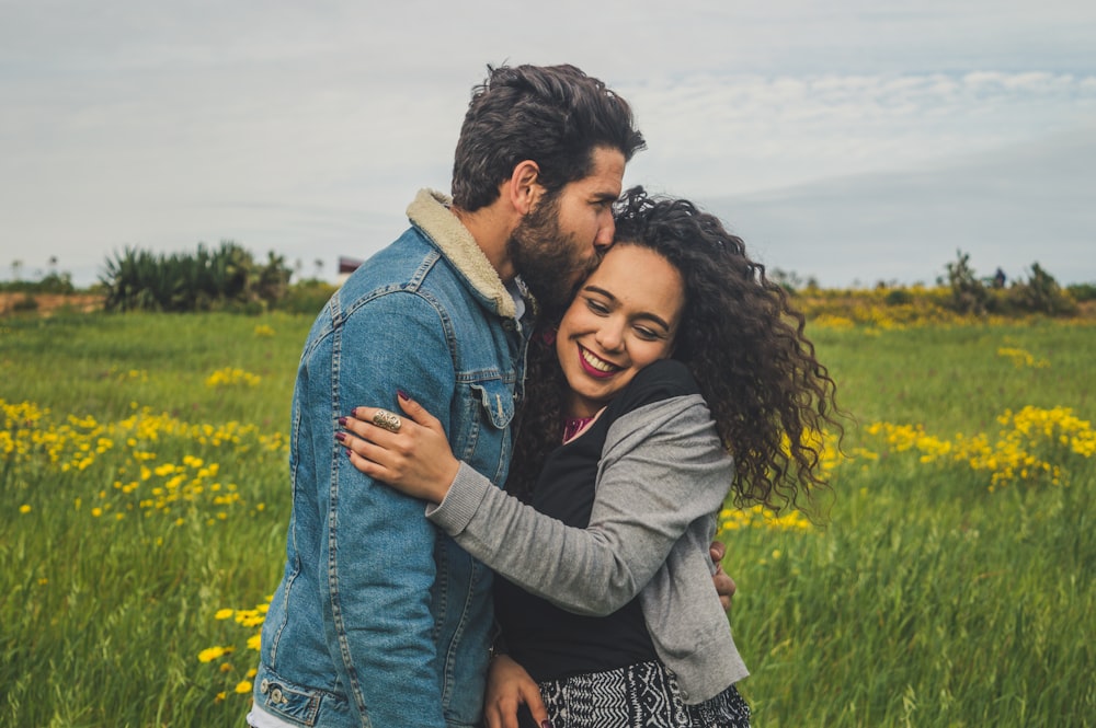 man kissing on woman's head on the green grassy field