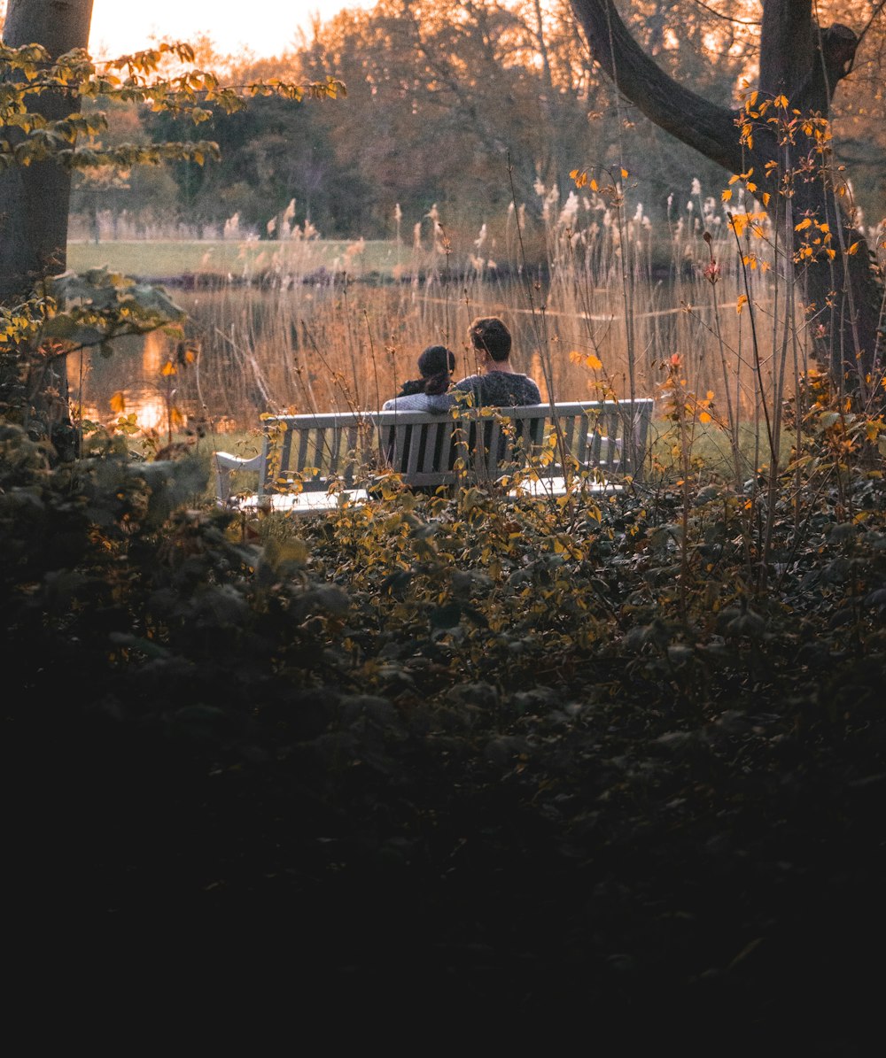 man and woman sitting on the bench facing the lake