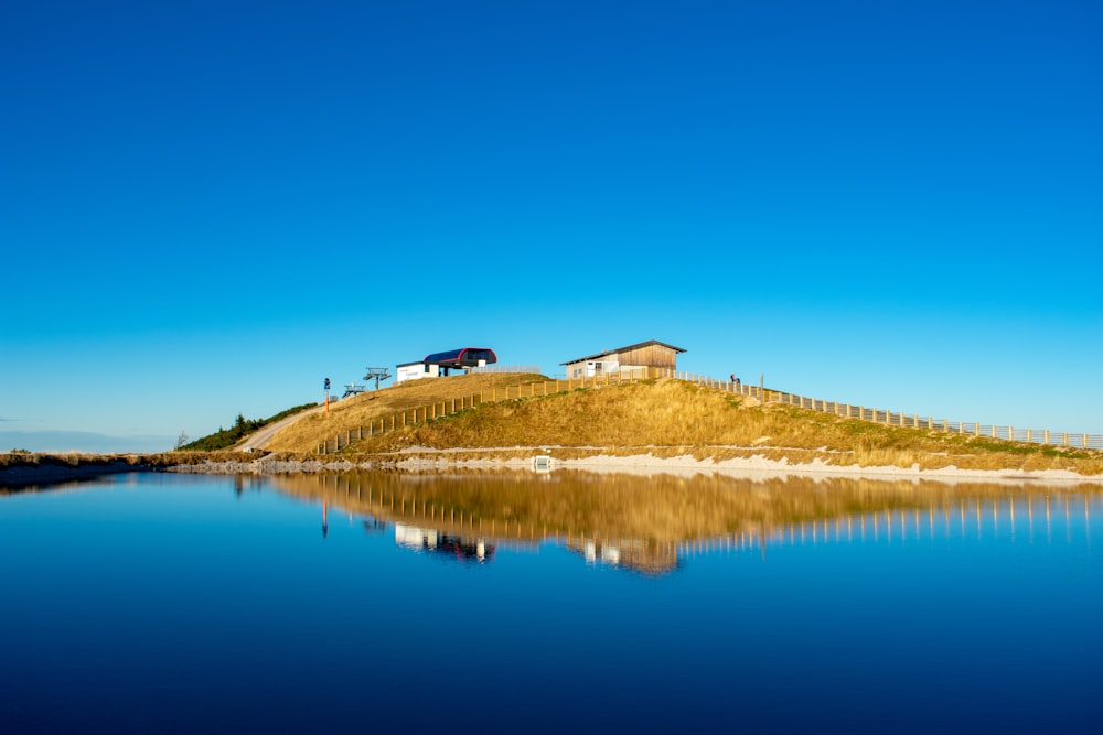 two buildings on green hill reflected on water under blue sky