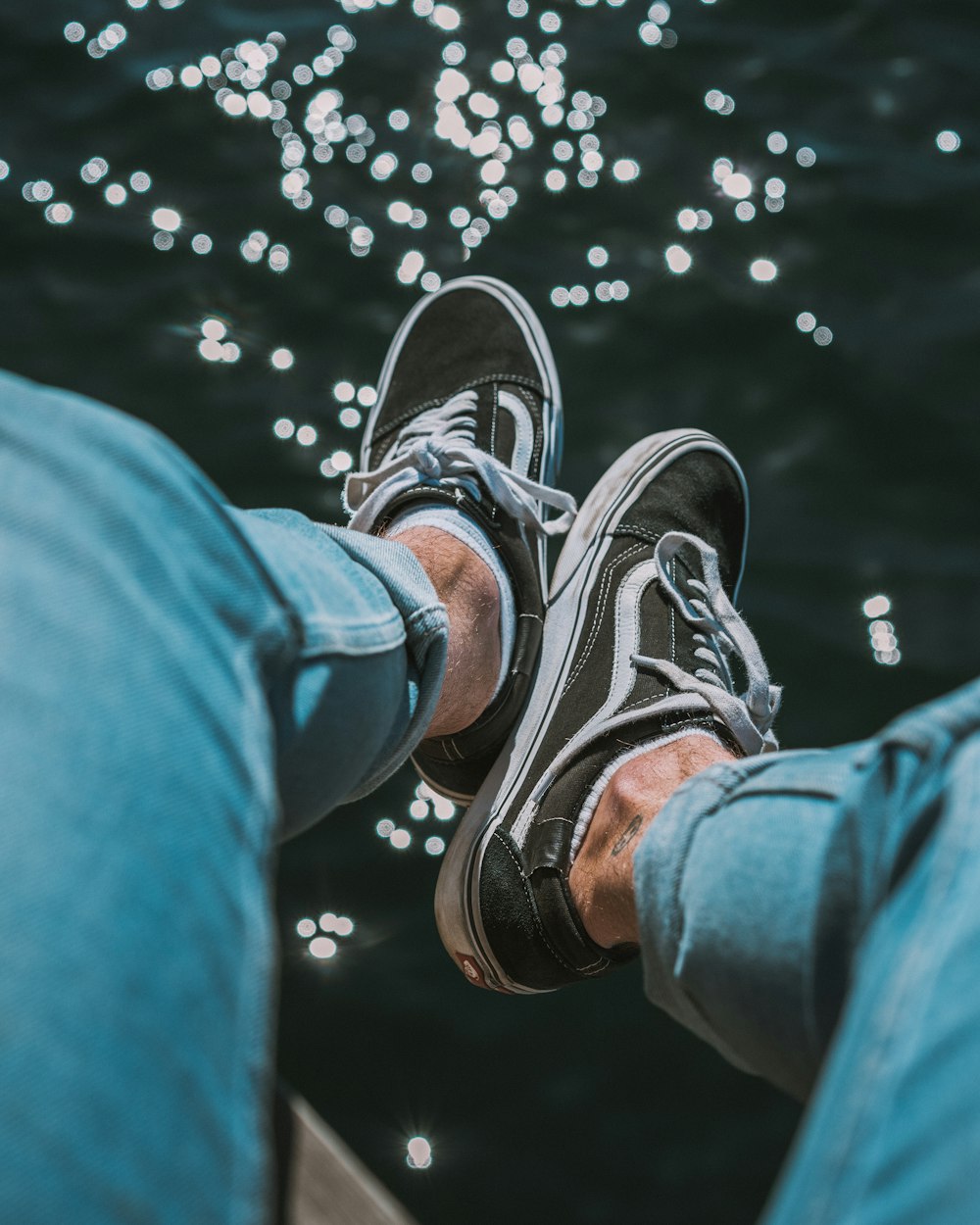 person in blue denim jeans wearing black and white Vans low-top sneakers