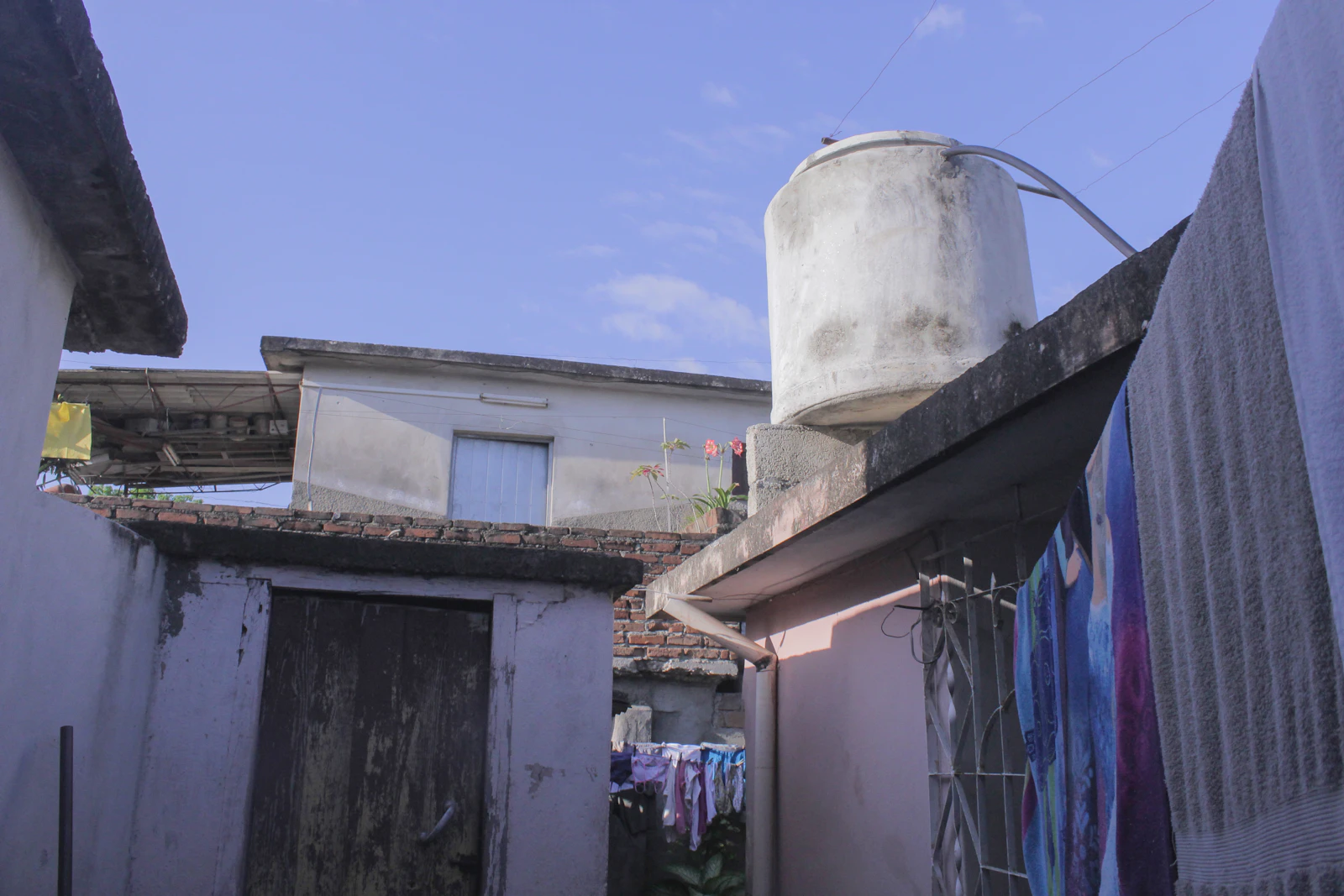 A white cylindrical water storage tank mounted on a rooftop ledge, the kind of exposed tank that bakes in direct sun on Kuwaiti villas through the long summer