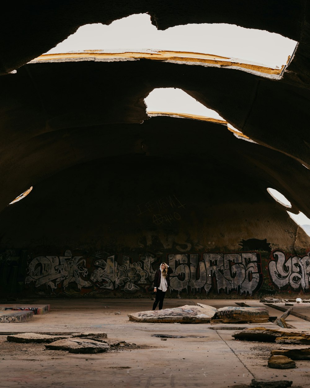 person standing under concrete dome building with holes on roof during daytime