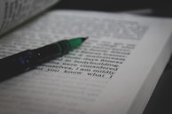 A journal open to a page of book reviews with a pen lying across it.