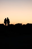 Sunset silhouette of newlyweds hugging on a rocky outcrop overlooking the valley.