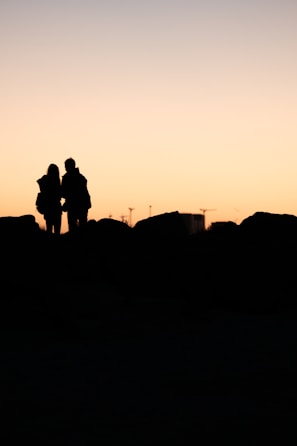 A silhouette of two people sharing a quiet, intimate moment at sunset.