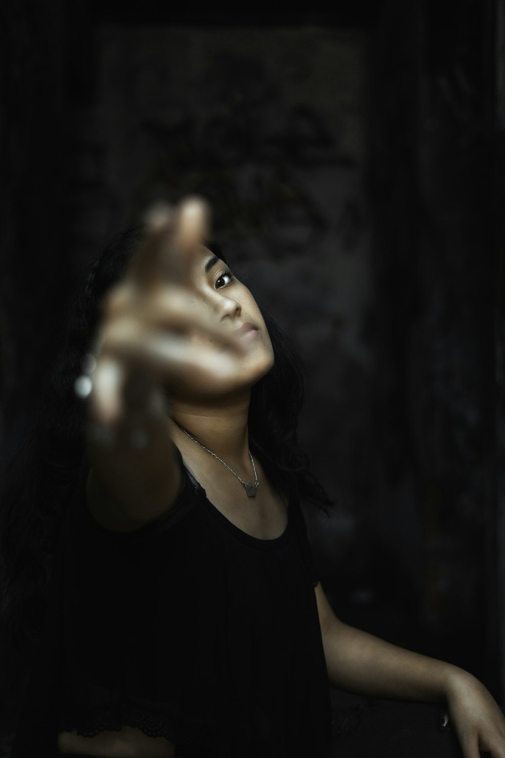 woman raising her right hand near grey wall