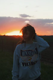 A person wearing a Lionsgear hoodie standing outdoors with a sunset backdrop.