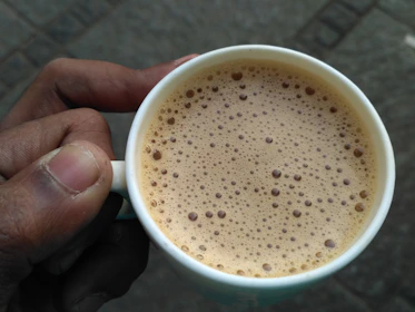 Hands holding a freshly brewed cup of coffee with a creamy foam top.