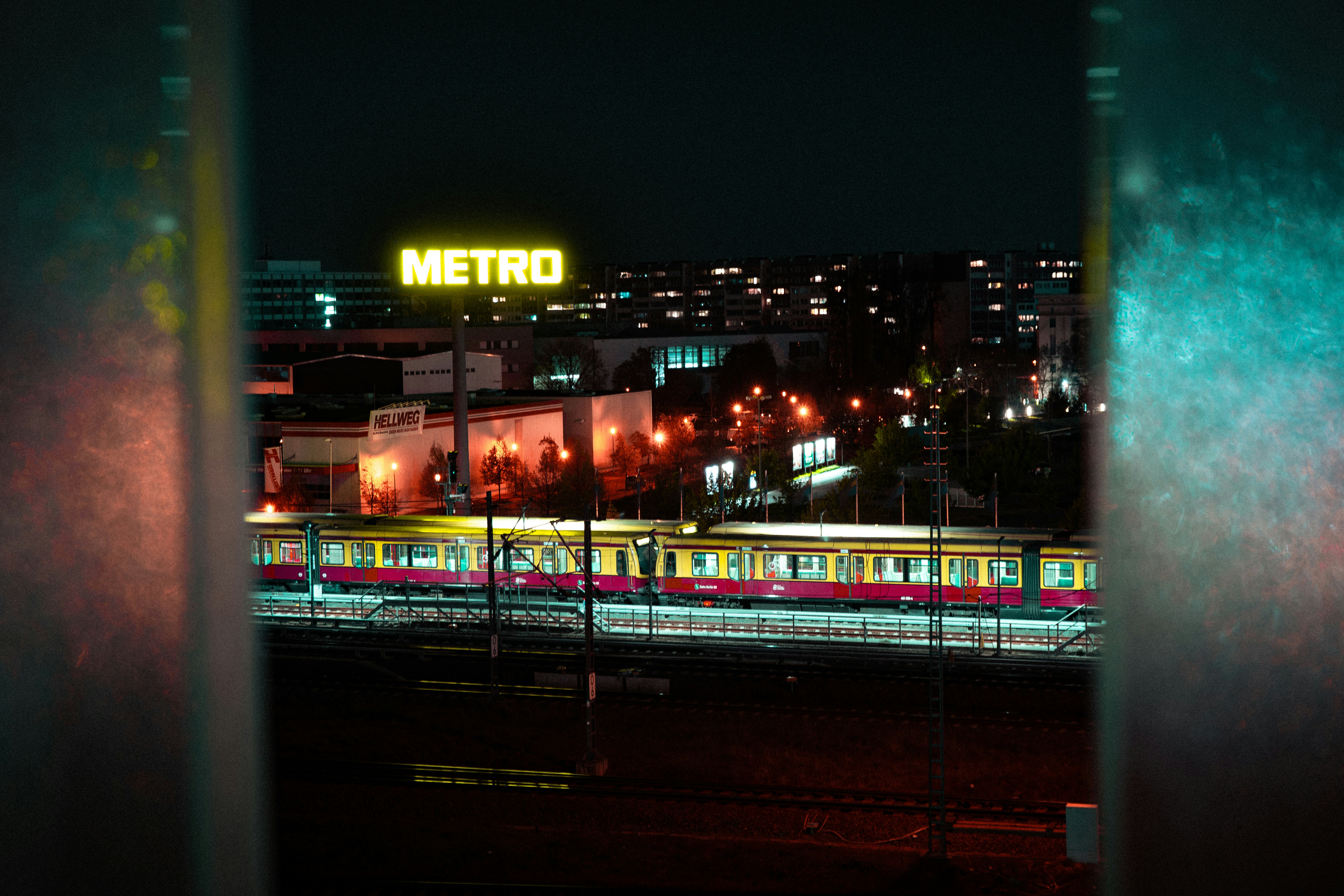 Nighttime metro train on tracks beneath a glowing METRO sign, with colorful reflections in the foreground.