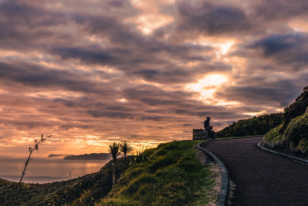 man sitting on bench near curved road during golden hour