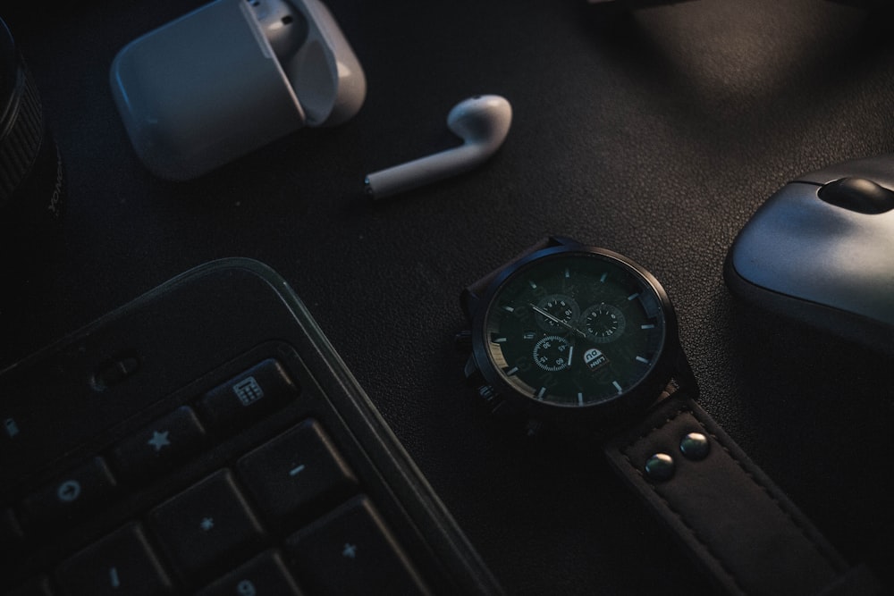 black chronograph watch beside AirPods and keyboard