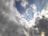 A dynamic sky scene featuring a mix of dark and light clouds with patches of blue sky peeking through. The clouds vary in thickness and texture, with some areas appearing more turbulent while others are softer. Sunlight creates a bright highlight on some clouds, enhancing the contrast and depth.