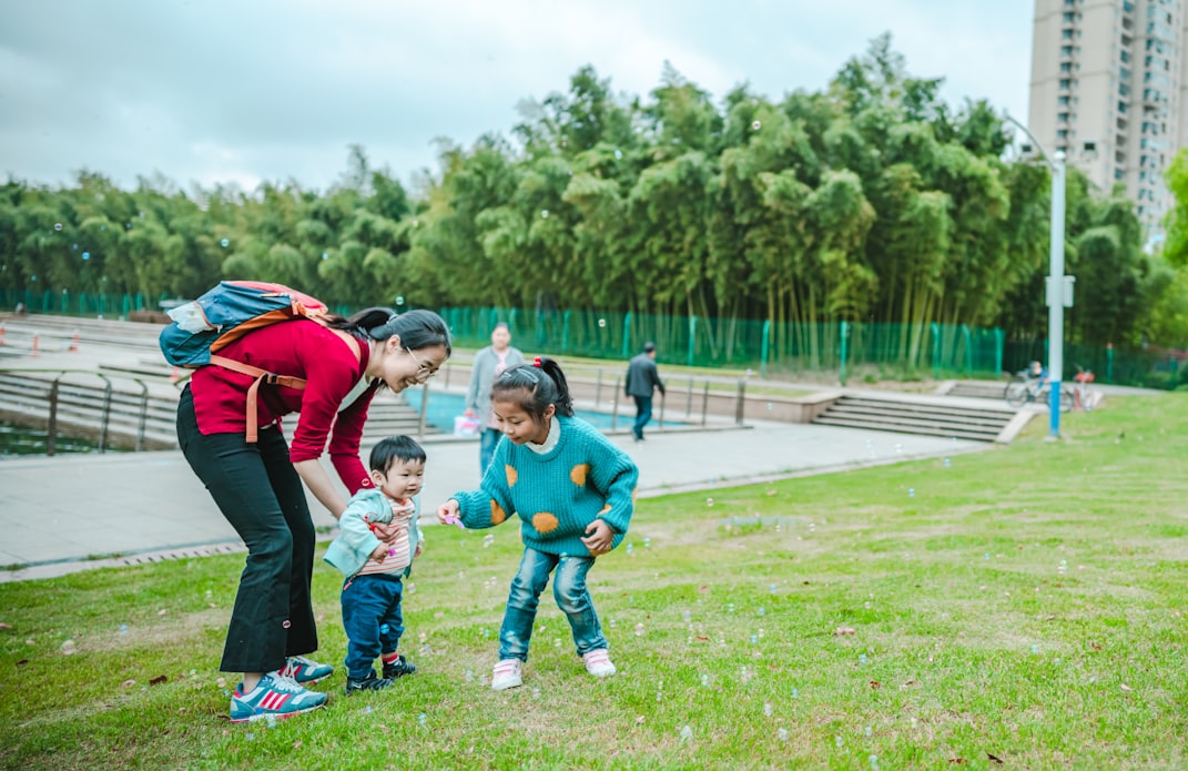 Uma mãe saindo da aula com sua filha segurando o seu filho em um parque.