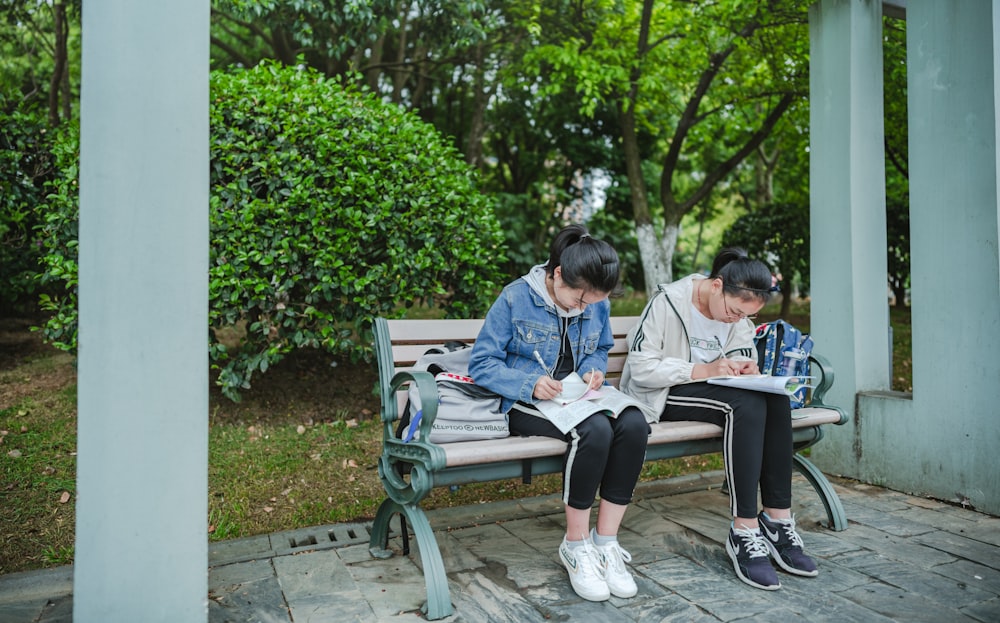 two people sitting on a bench writing on paper
