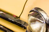 Close-up of a classic car's gleaming headlight reflecting a mountain landscape.