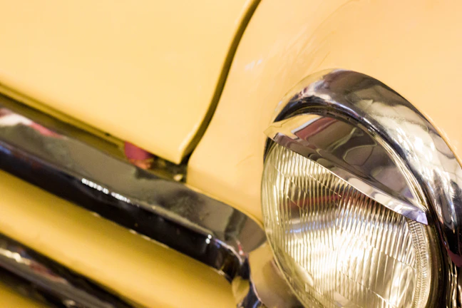 Close-up of a classic car's gleaming headlight reflecting a mountain landscape.