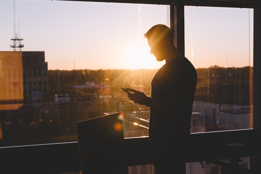 man holding phone beside glass window