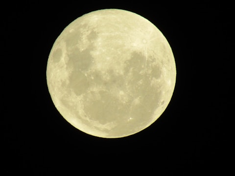 A full moon is prominently displayed against a dark night sky, showcasing its detailed surface with visible craters and shading.