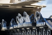 Close-up view of a series of metal components with a rugged, industrial appearance. The elements have a cylindrical tip, structured in a row along a mechanical part, likely part of heavy machinery such as a trencher or drilling equipment. The background is softly blurred, focusing attention on the sharp and metallic texture of the components.