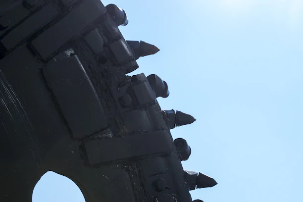 Close-up of a rugged rock drill bit mounted on heavy mining equipment against a dark industrial background.