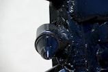 A close-up view of a metallic machine part with a prominent cylindrical feature. The surface is dark and glossy, with visible welds and textural details on the surrounding metal.