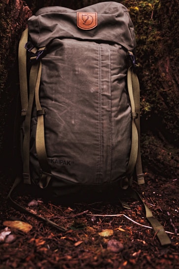 A rugged, large-capacity men's outdoor backpack in earth tones, resting against a forest backdrop.