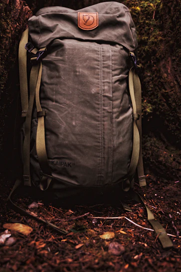 Close-up of a rugged green jungle backpack with the žali keliai logo embroidered on the strap, resting on moss-covered rocks.