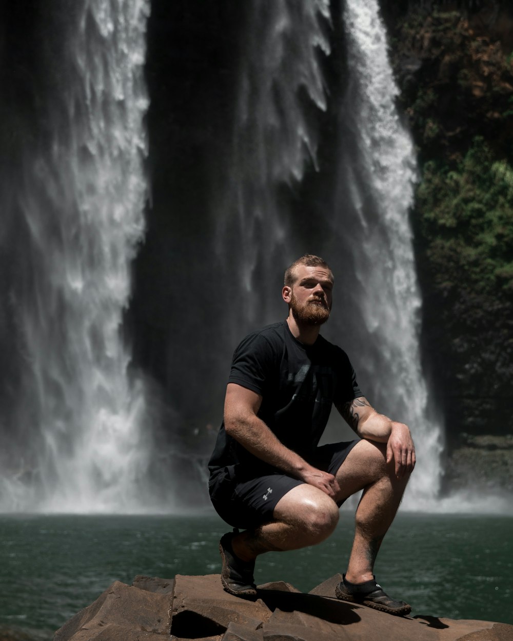 man sitting on rock near waterfalls