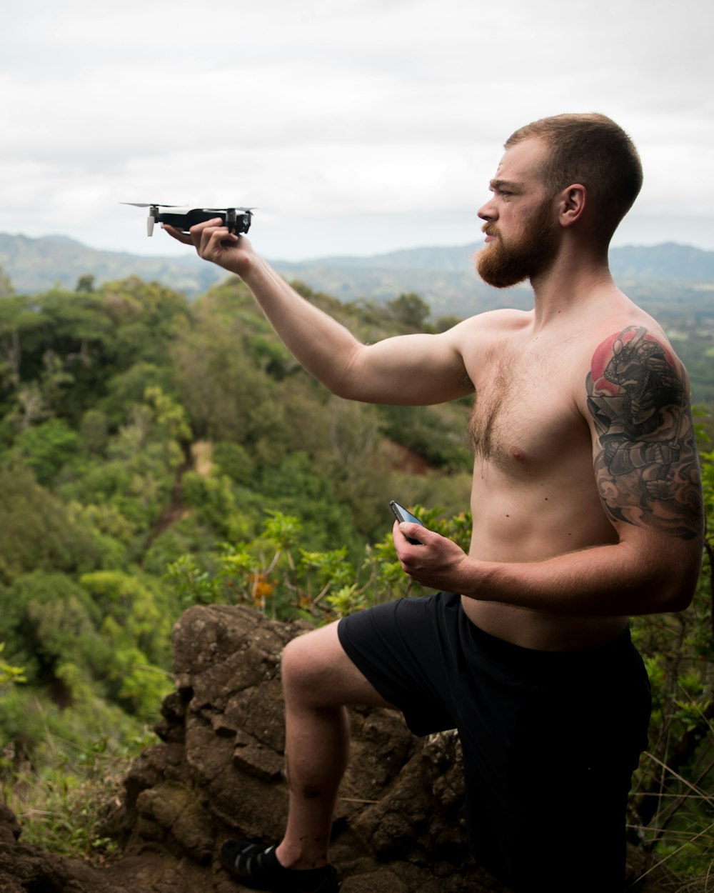 half naked man on top of rock holding drone