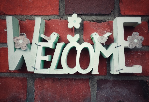 A charming outdoor welcome sign hanging on a rustic wooden door surrounded by greenery.
